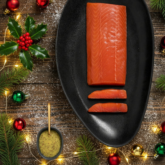 A fillet of smoked salmon on a black plate with a small dish of seasoning on the side, all presented on a wooden surface.