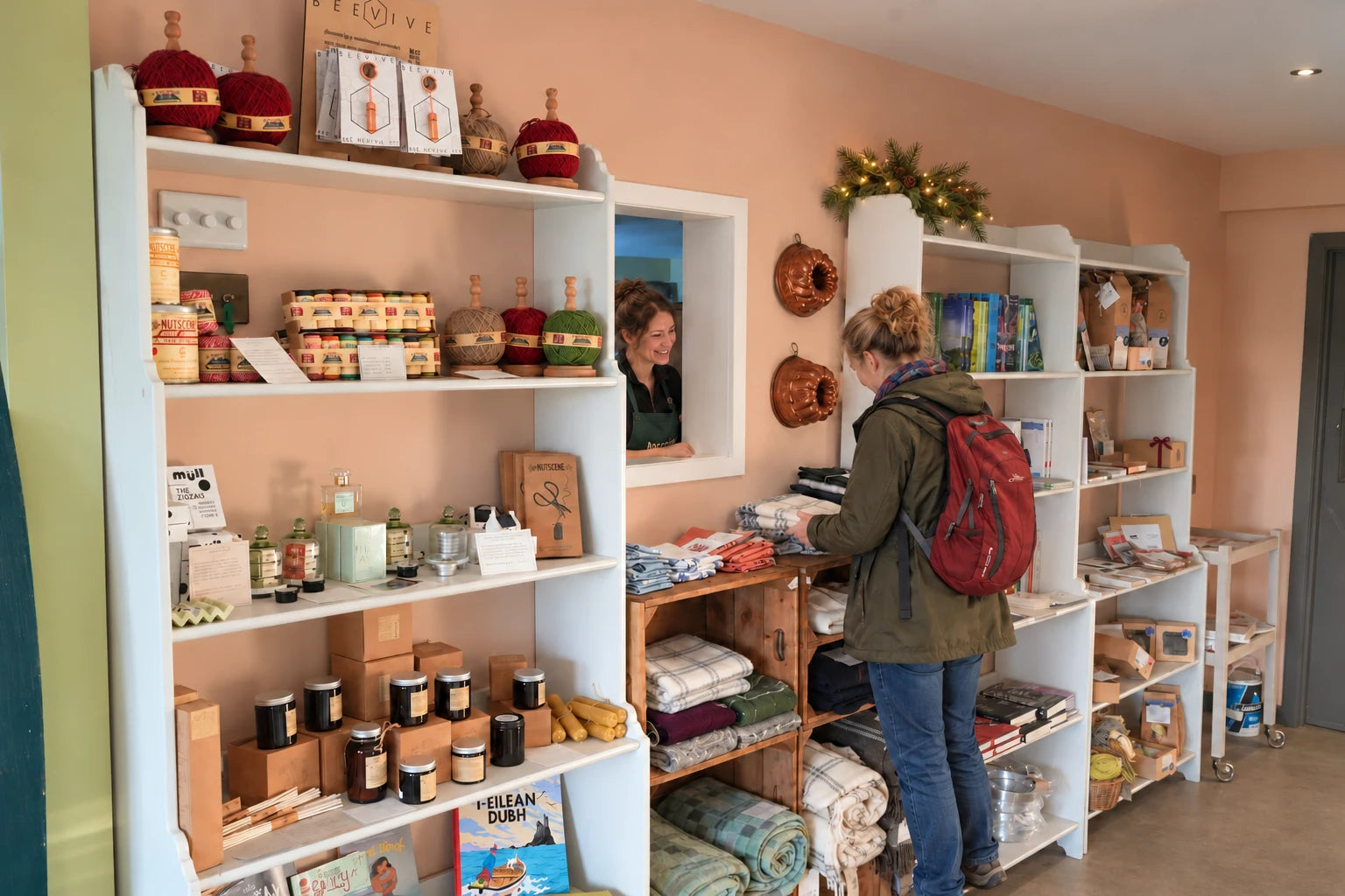 A customer browsing textiles and gifts in the Inverawe shop, with understated festive greenery on the shelves.